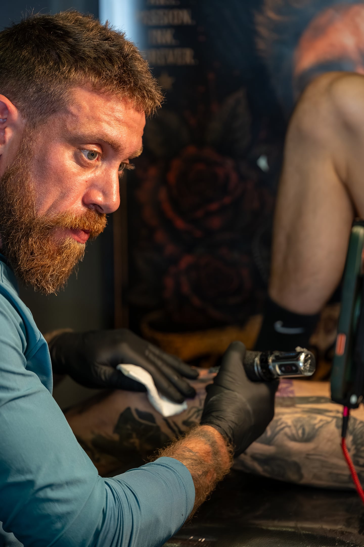 A bearded tattoo artist concentrating on a client's arm.