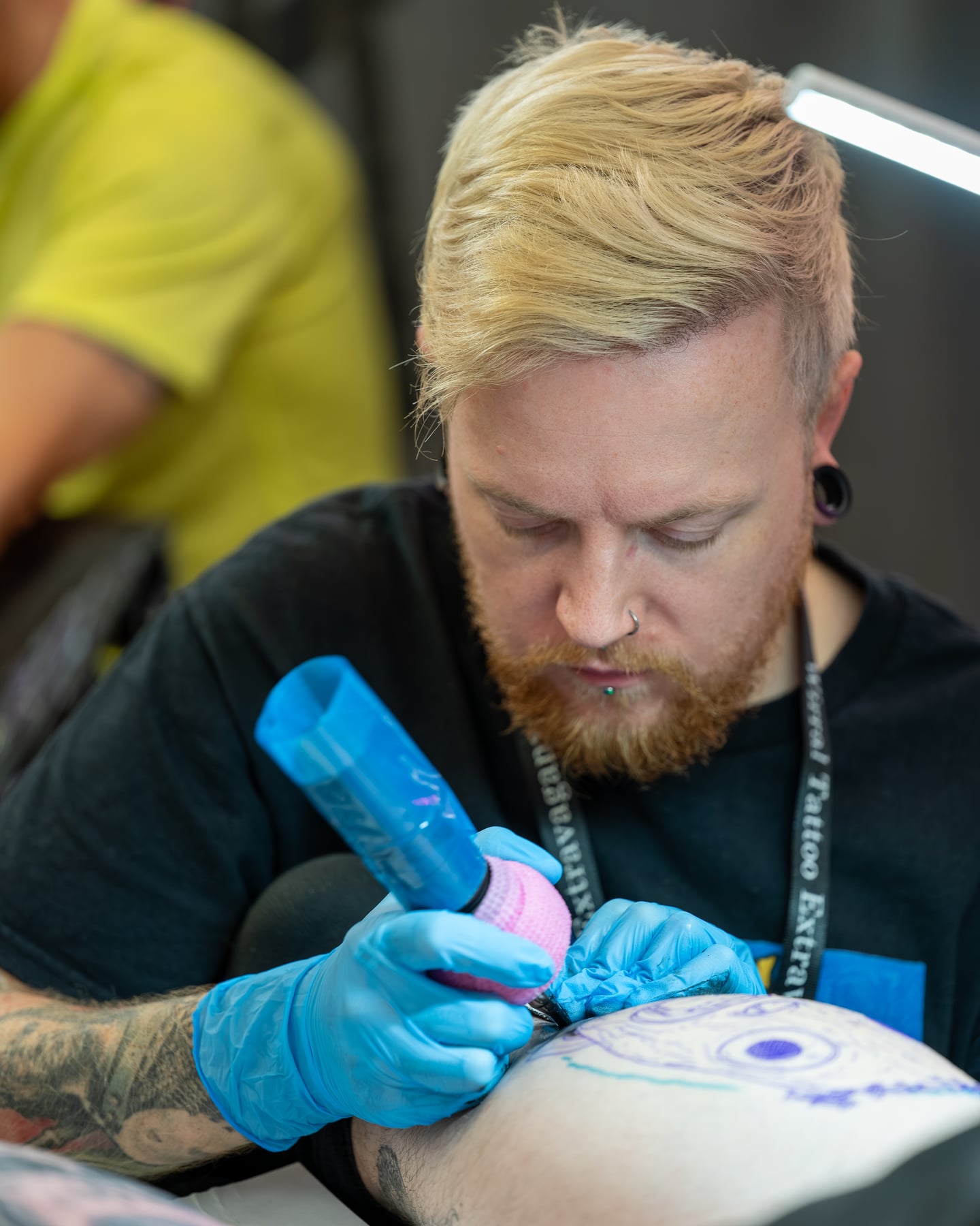 A blond tattoo artist concentrating while working with blue gloves.