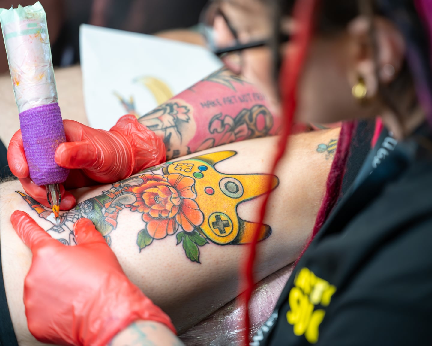 A tattoo artist in red gloves working on a colourful floral design.