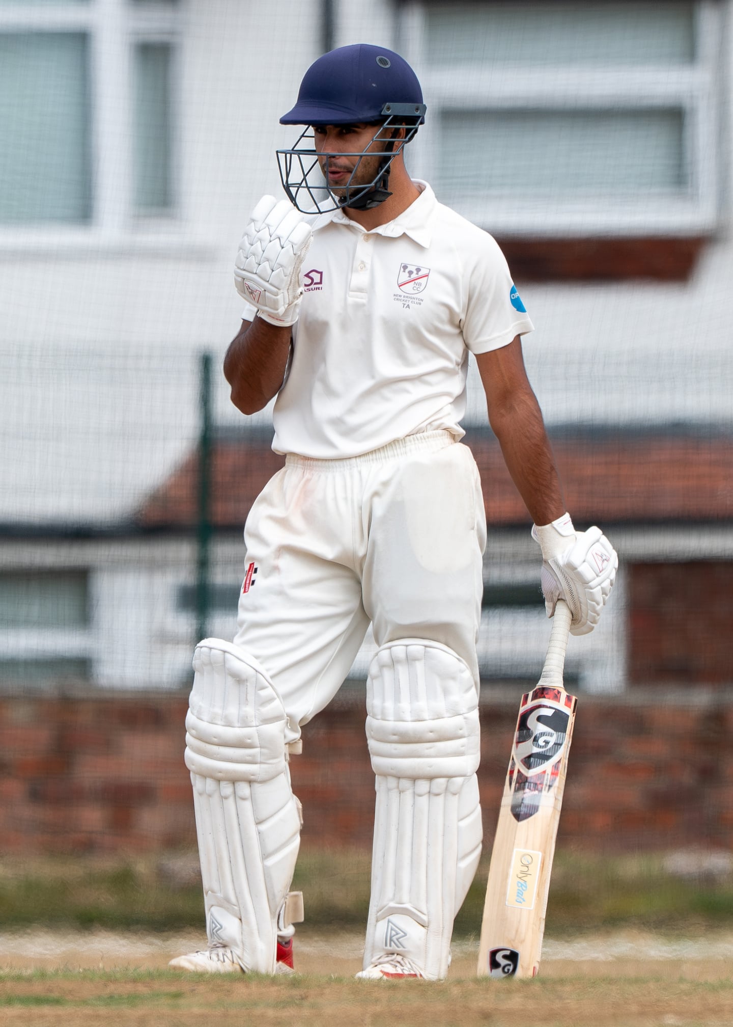 A cricket batter in a dark helmet holding a bat between deliveries.