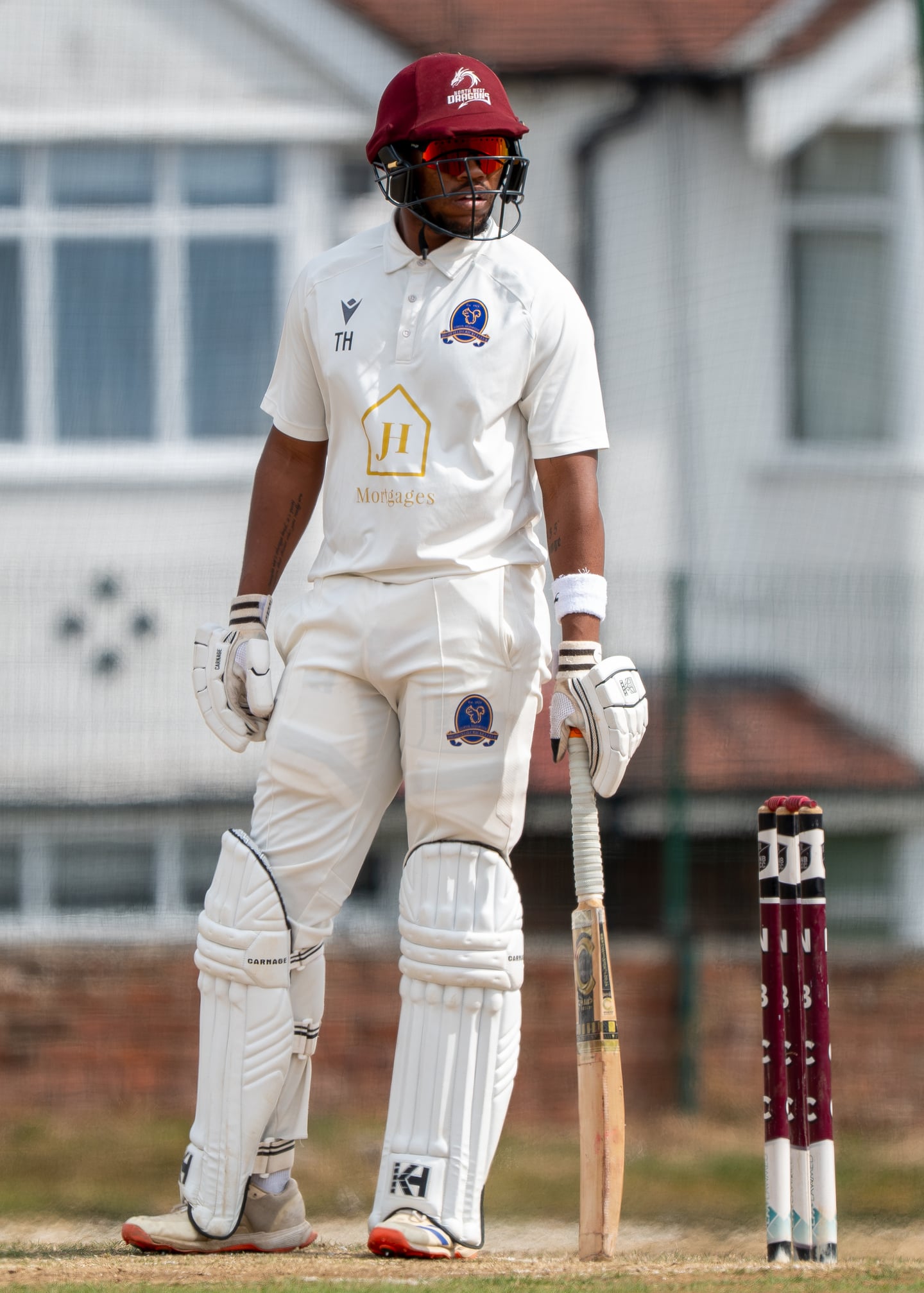 A cricket batter in a red helmet standing beside the stumps.