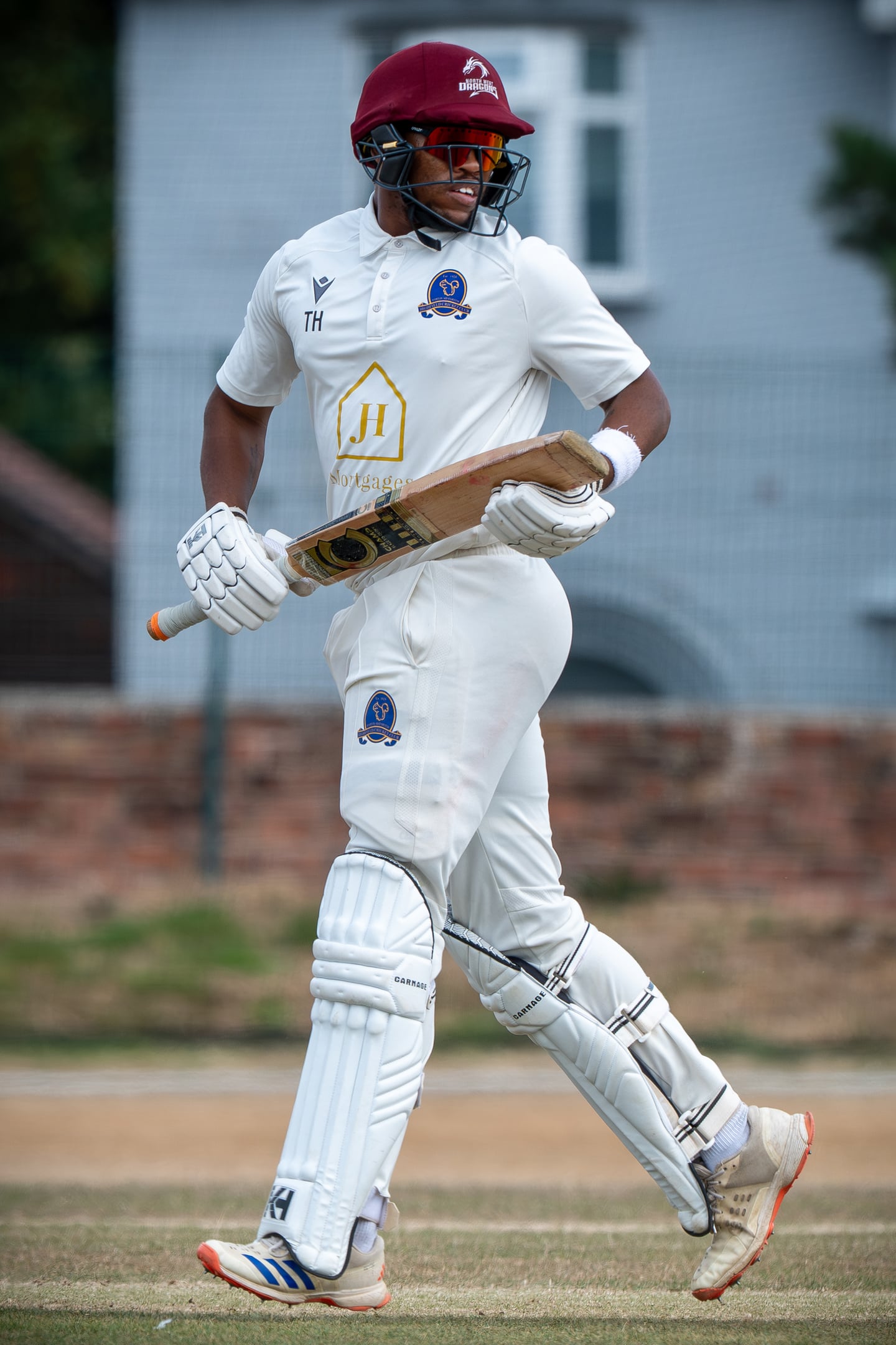 A cricket batter in a red helmet running with a bat.