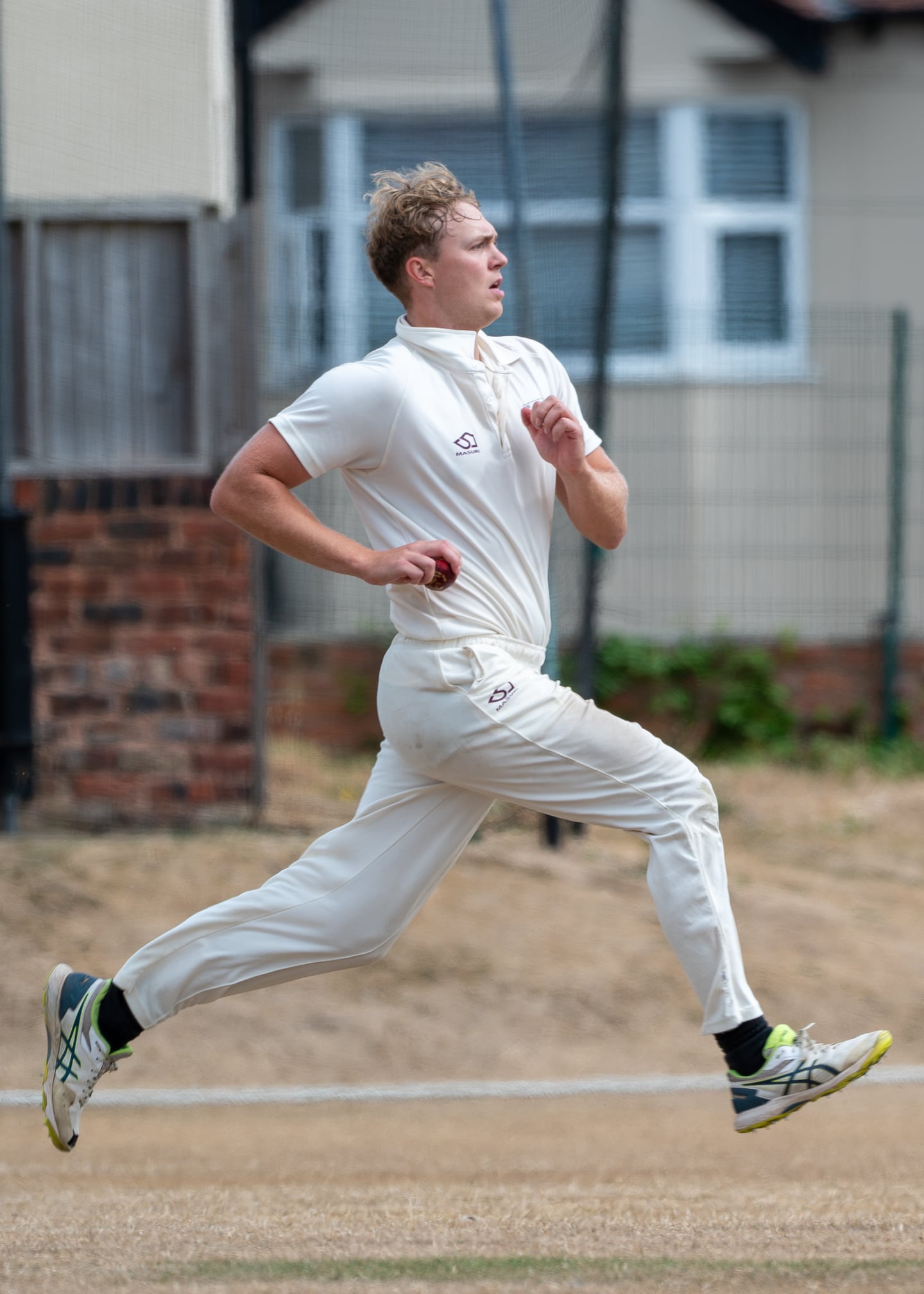 A cricketer in white running towards the crease with the ball.