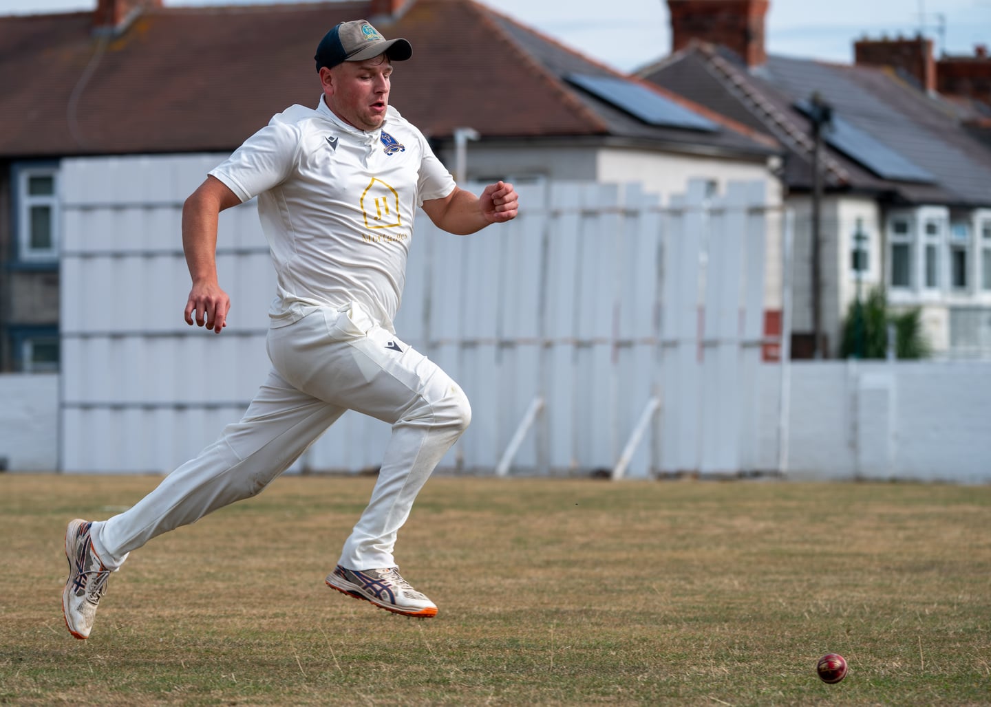 A cricketer sprinting after a ball across the grass.