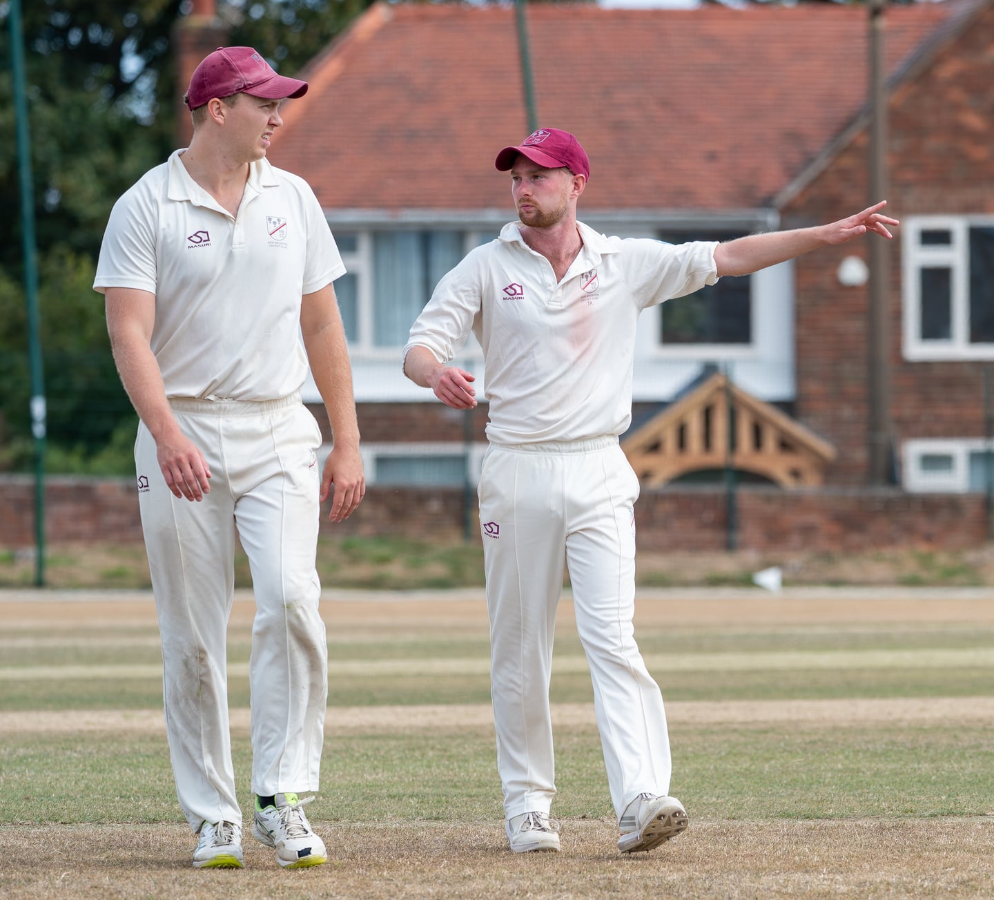Two cricketers in red caps talking between deliveries.
