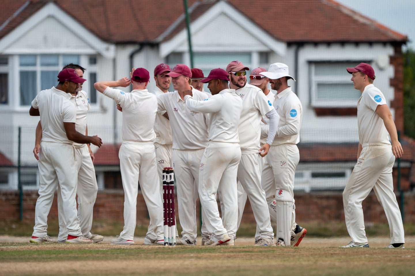 Cricketers in white gathering to celebrate on the pitch.