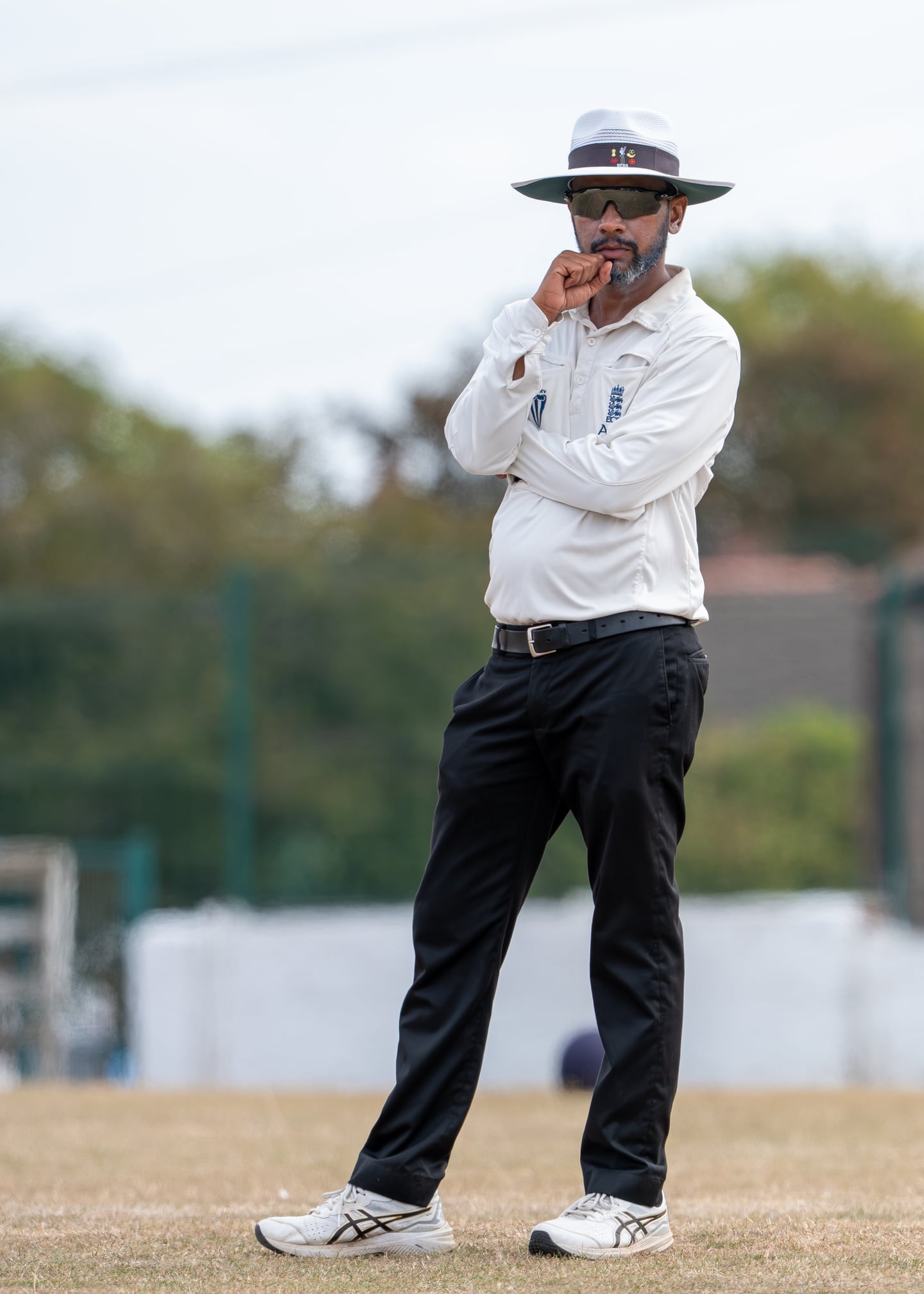 A cricket umpire in a white shirt and sun hat watching play.