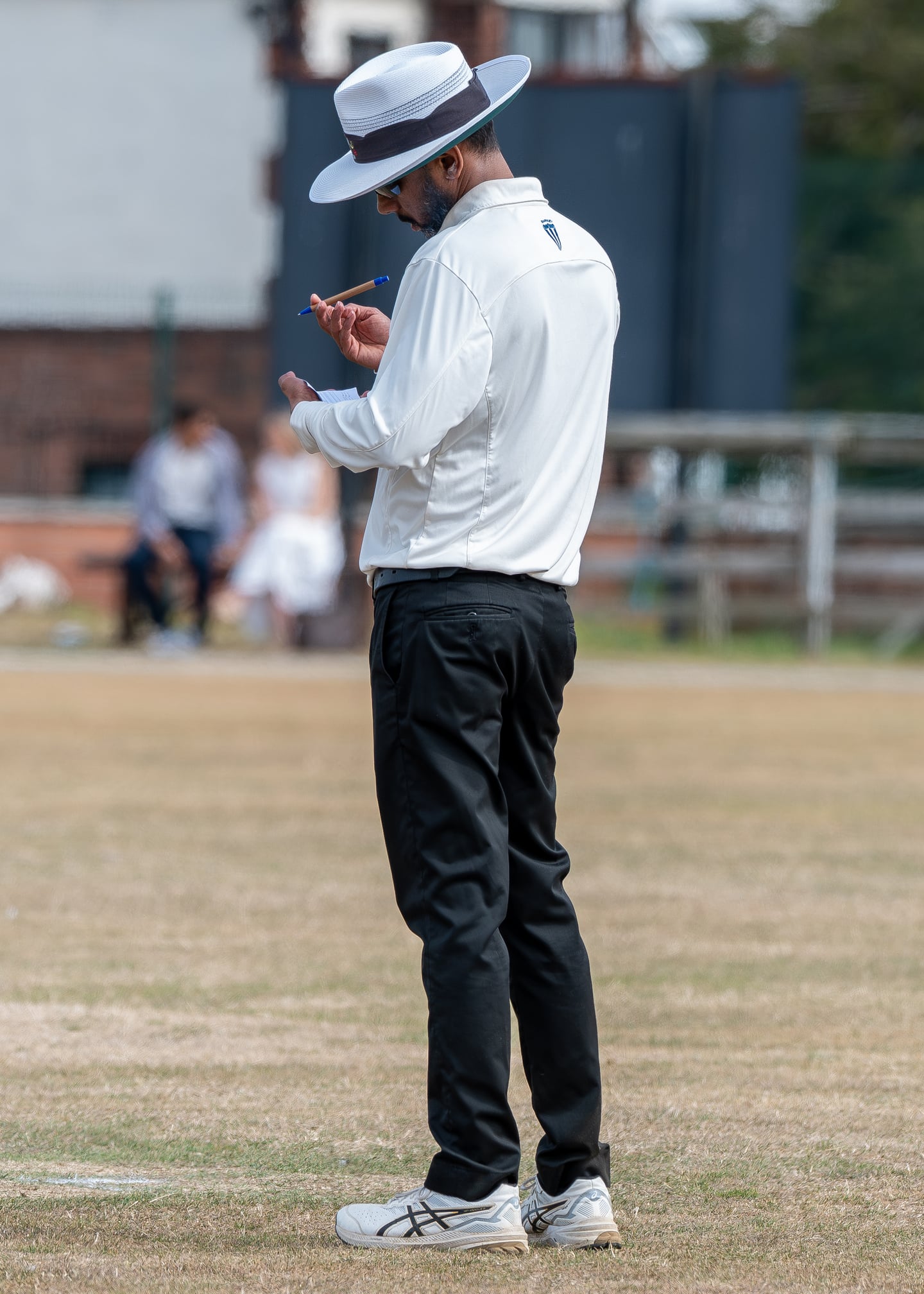 A cricket umpire looking down at their hands beside the pitch.