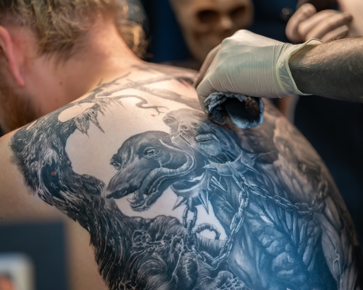 Gloved hands working on a detailed dragon tattoo across a client's back.