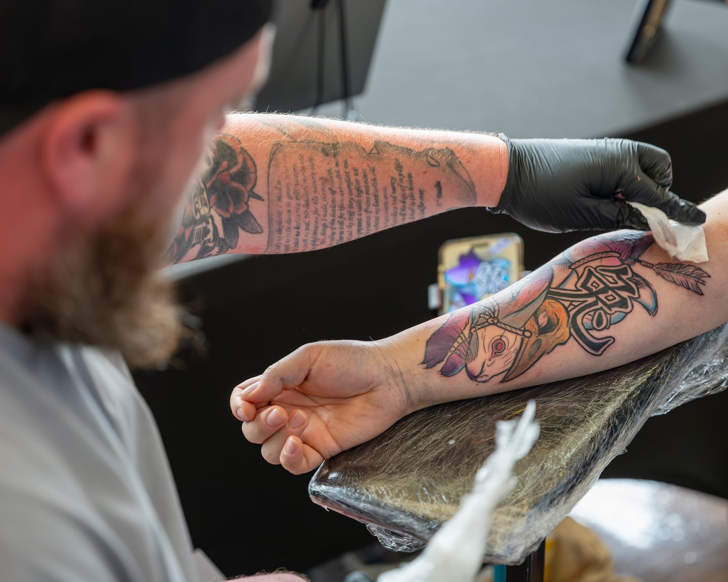 A tattoo artist wiping a colourful design on a client's forearm.
