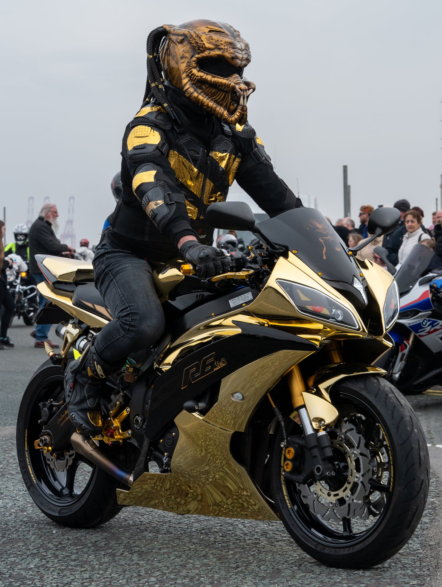 A rider in black and gold gear seated on a matching motorcycle.