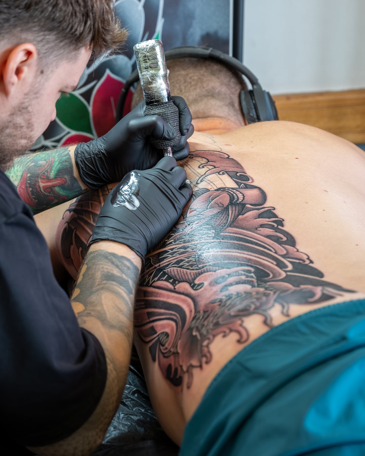 A tattoo artist working on a large design across a client's back.