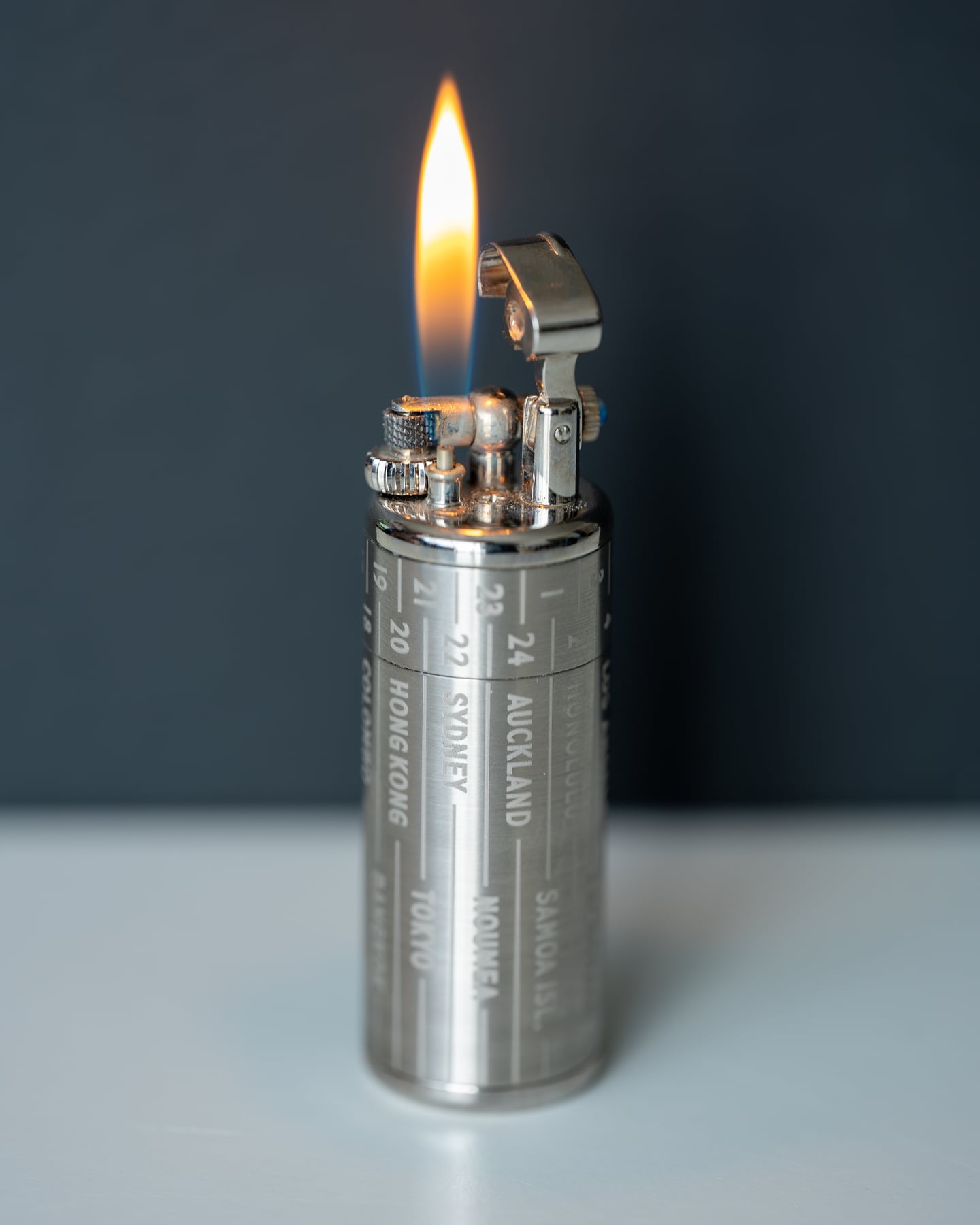 A metal lighter with a steady flame against a grey backdrop.