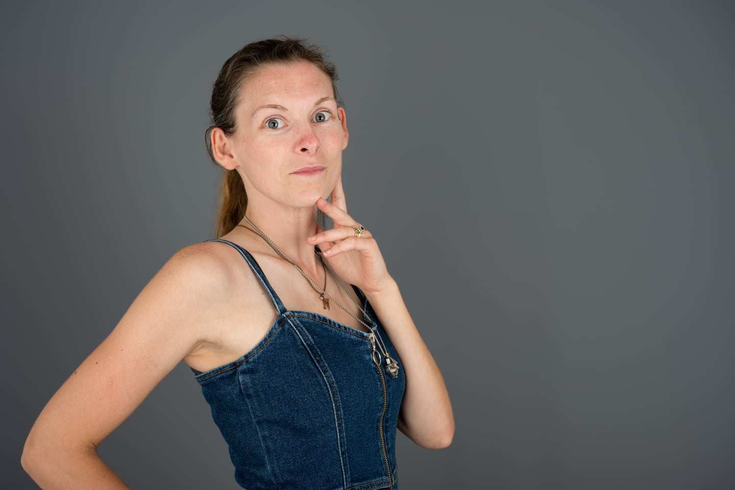 A model in a denim top posing against a grey studio backdrop.