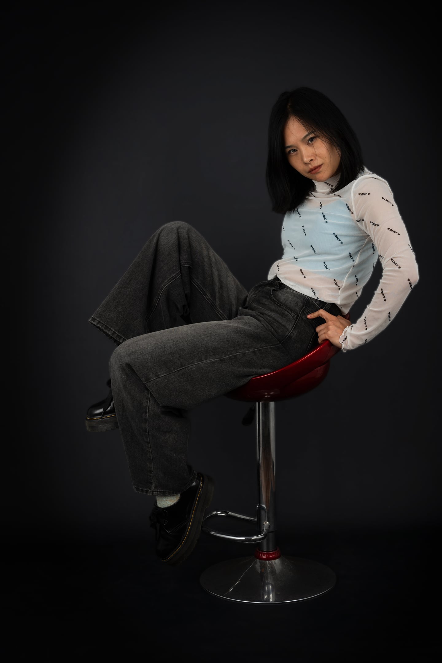 A model in a pale patterned top and dark trousers reclining on a studio stool.