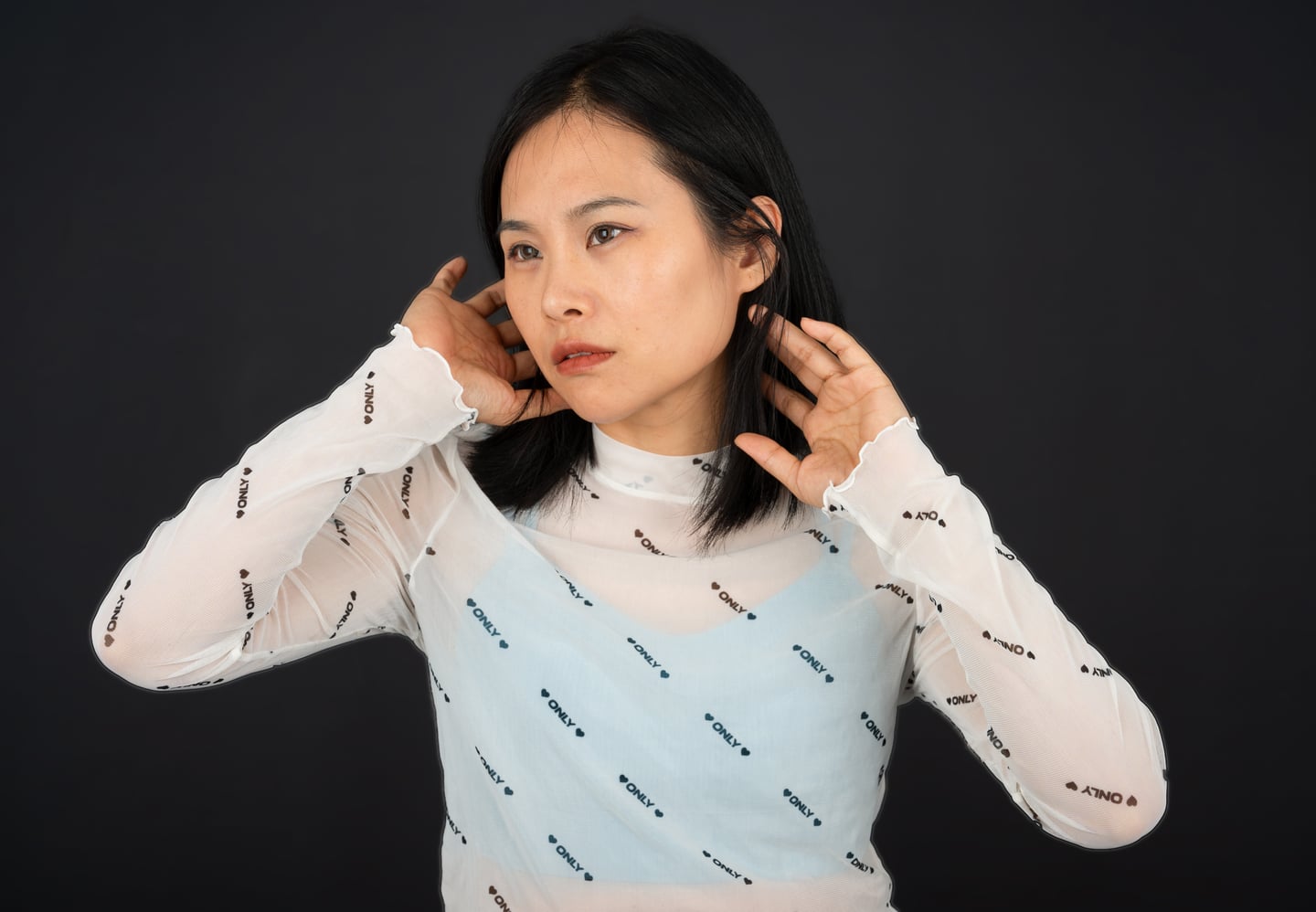 A model adjusting her hair against a dark studio backdrop.