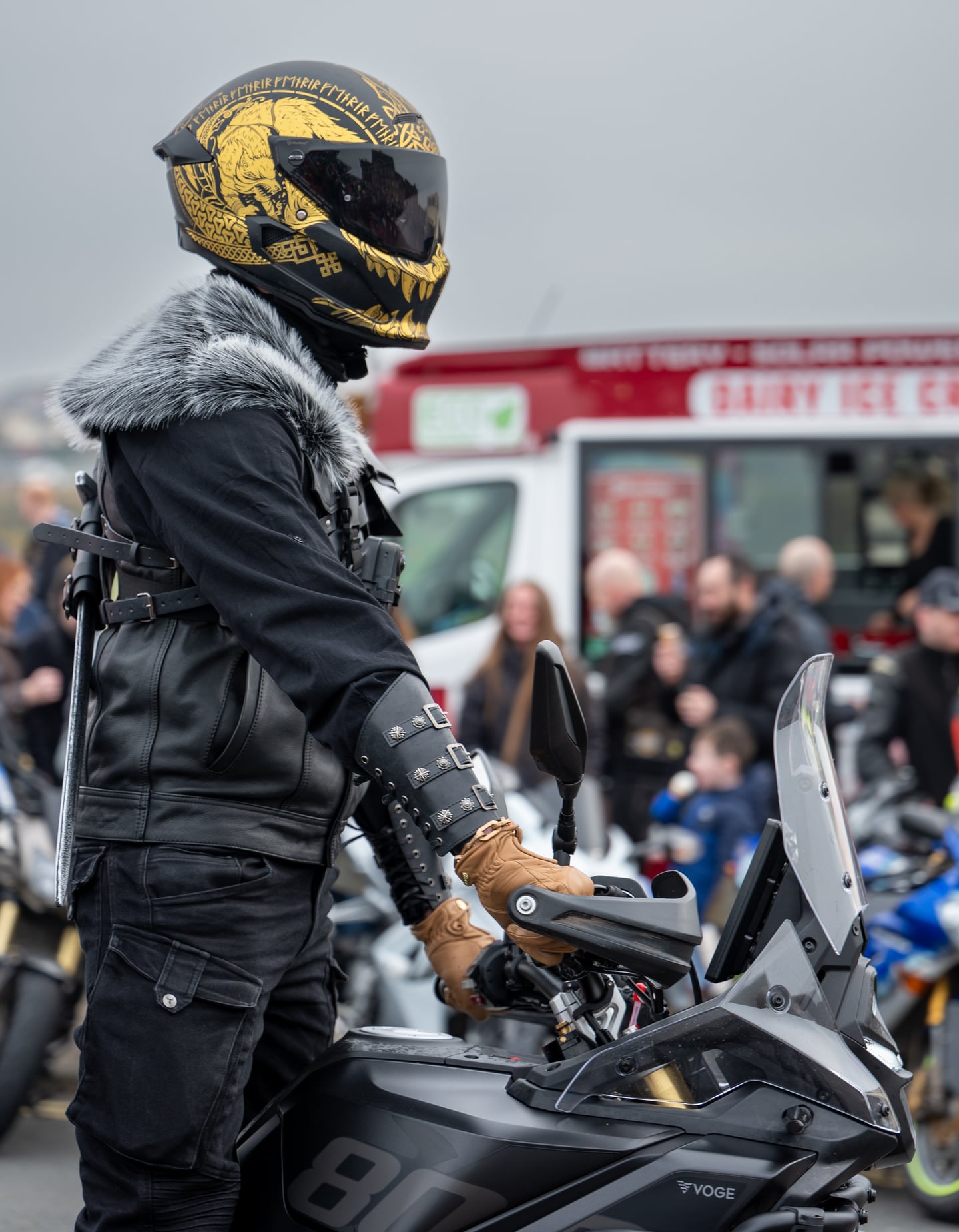 A motorcycle rider wearing a gold and black helmet at a gathering.