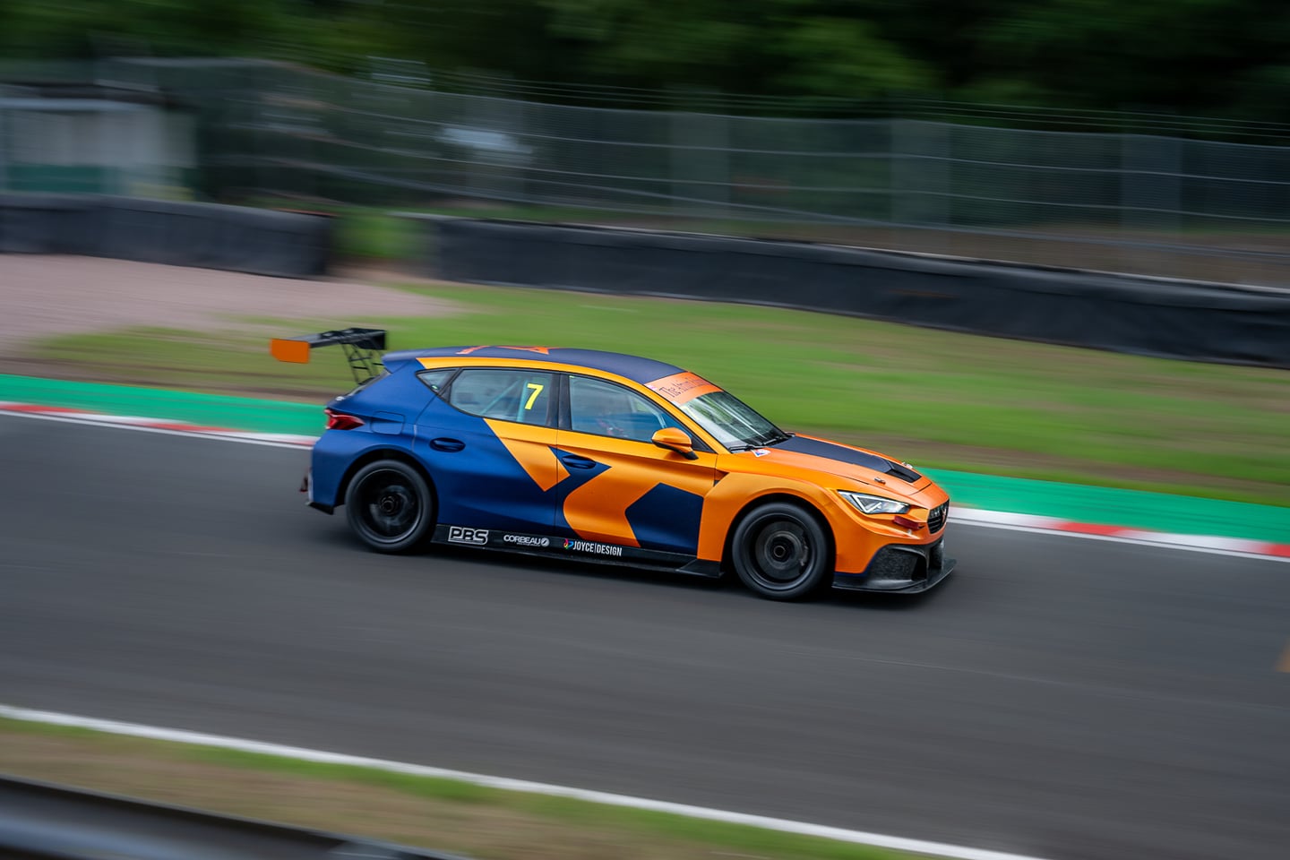 An orange and blue racing car passing the trackside barriers.