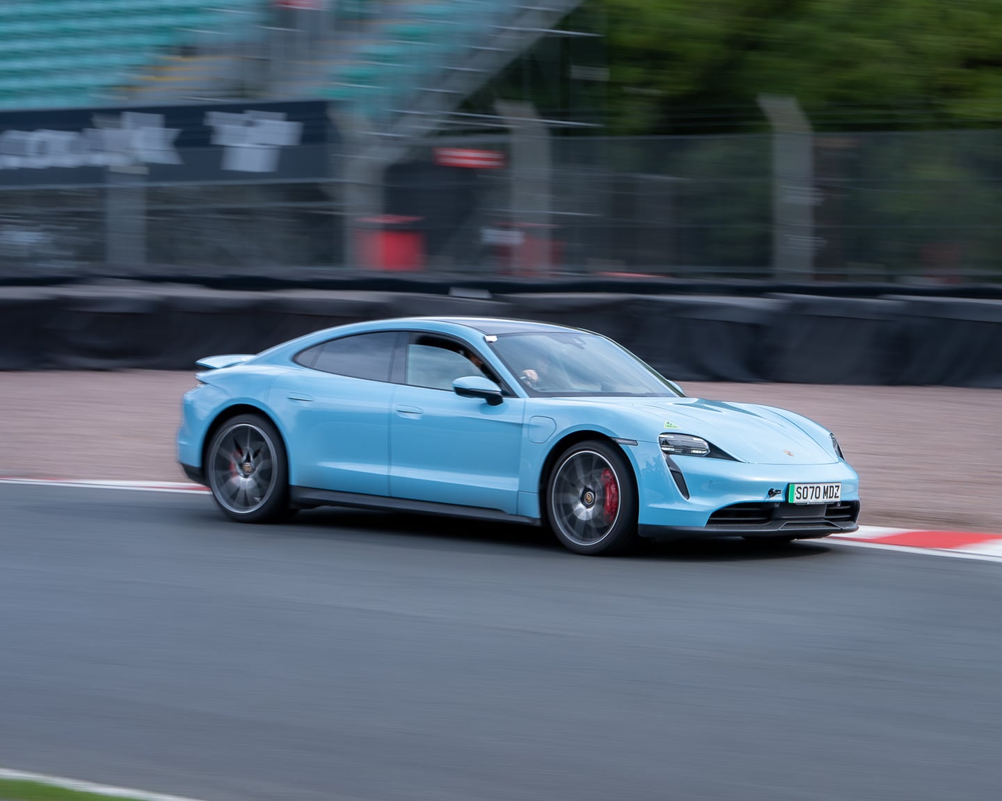 A pale blue sports car driving along a race circuit.