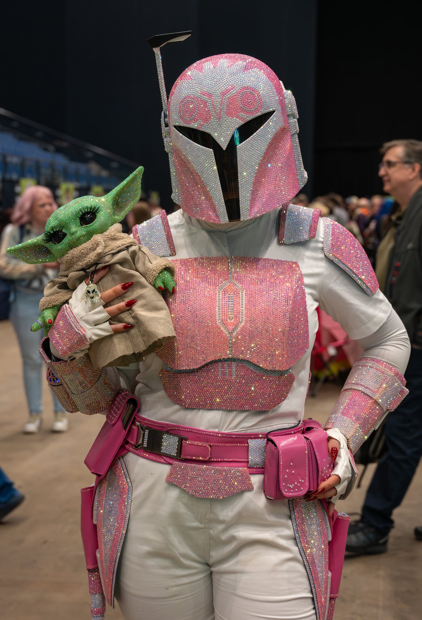 A convention attendee in pink armour holding a small green character figure.