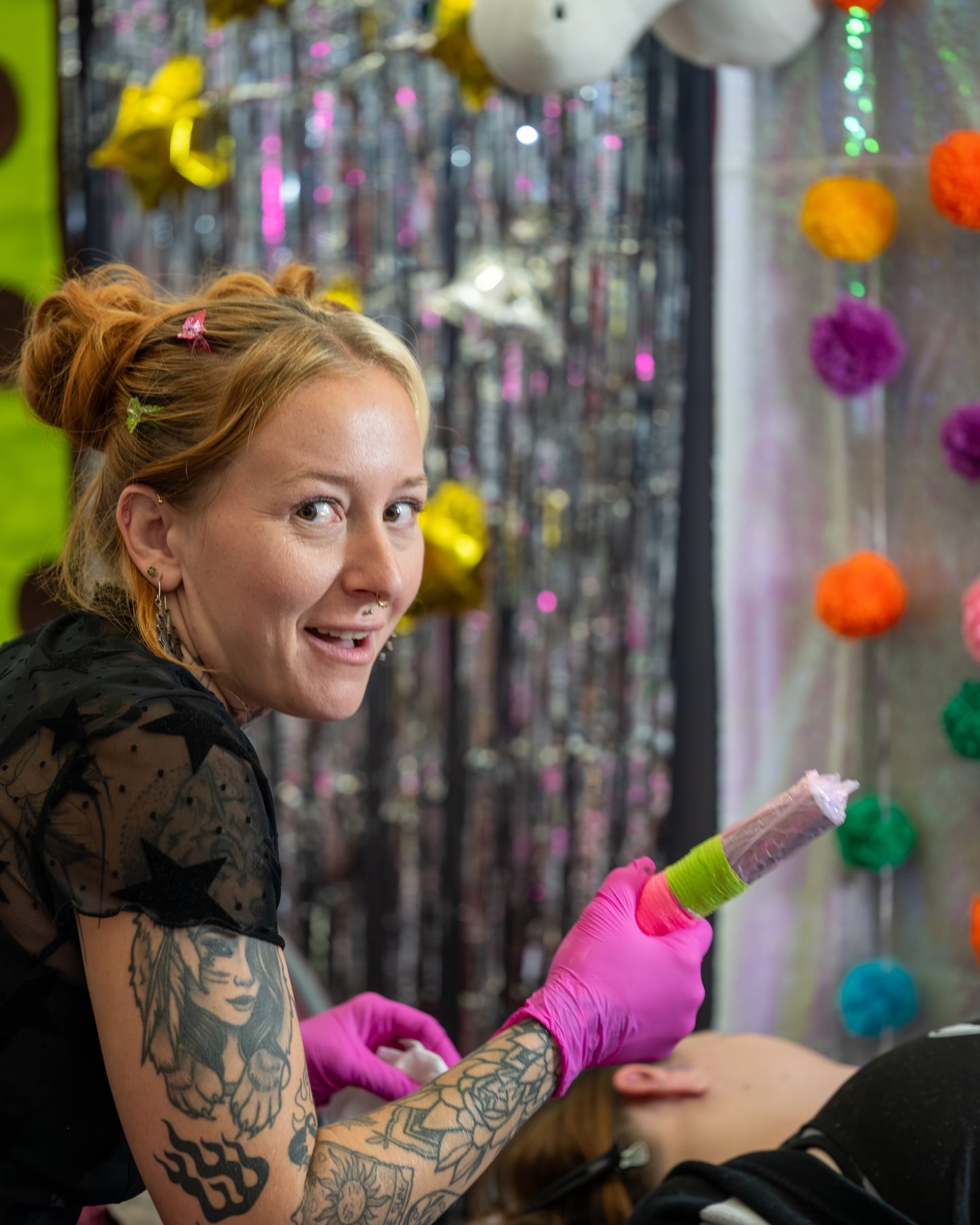 A smiling tattoo artist holding a machine with bright pink gloves.
