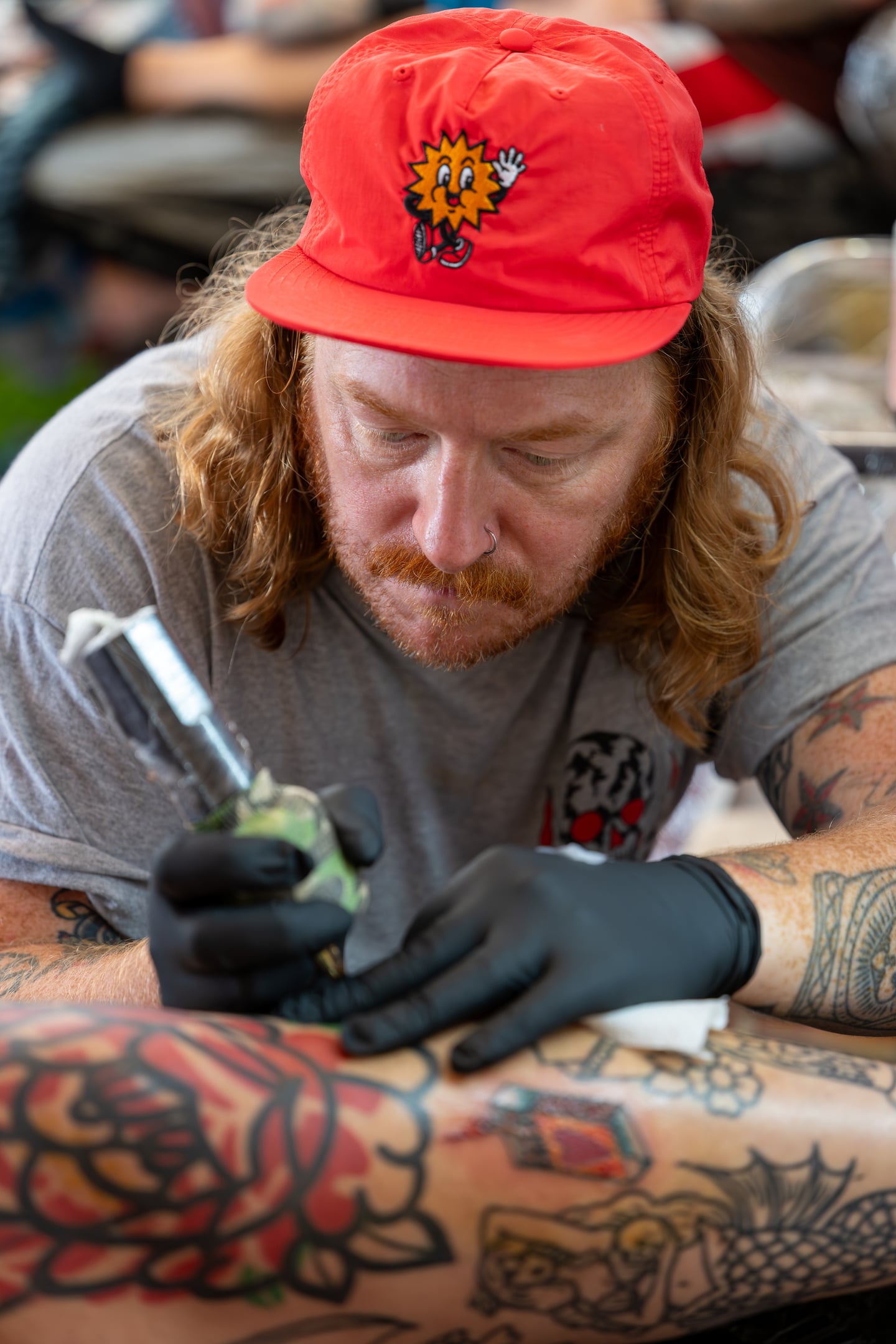 A tattoo artist wearing a red cap leaning over a colourful arm tattoo.