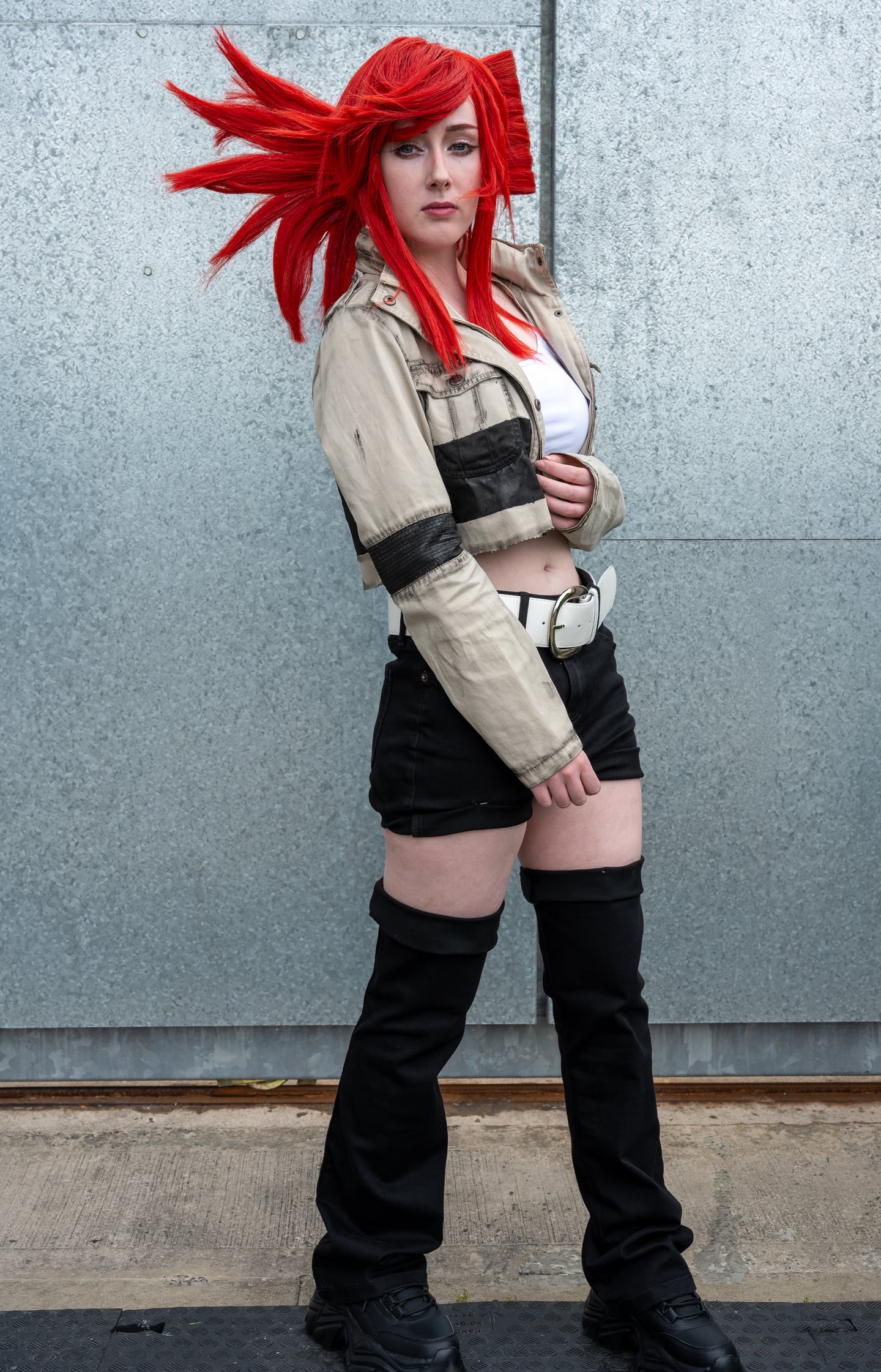 A red-haired cosplayer posing against a grey stone wall.