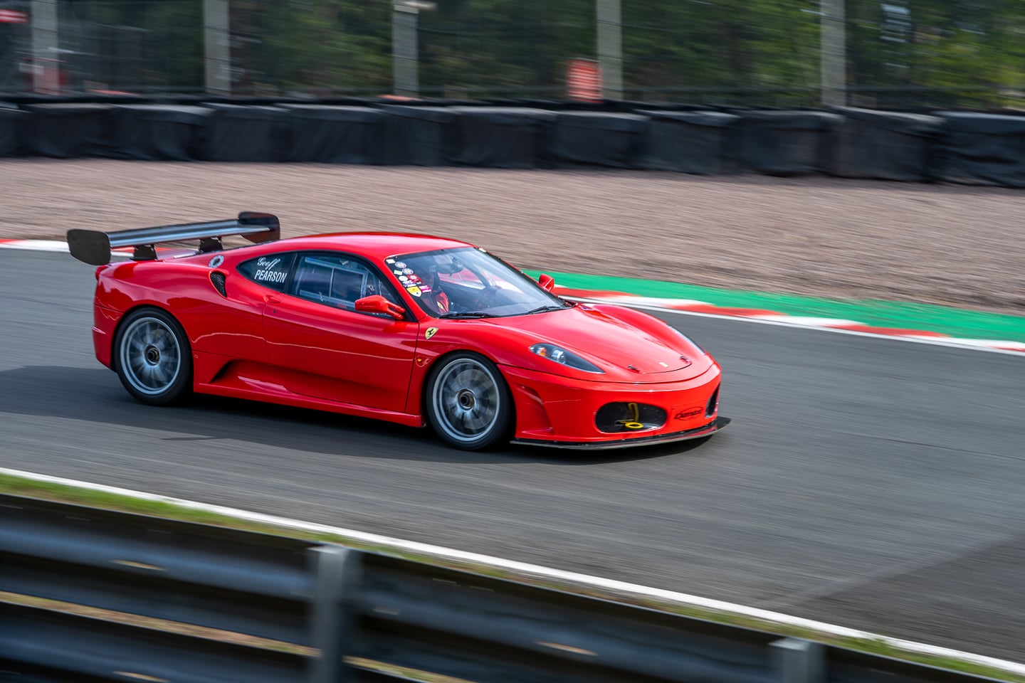 A red sports car passing trackside barriers at speed.