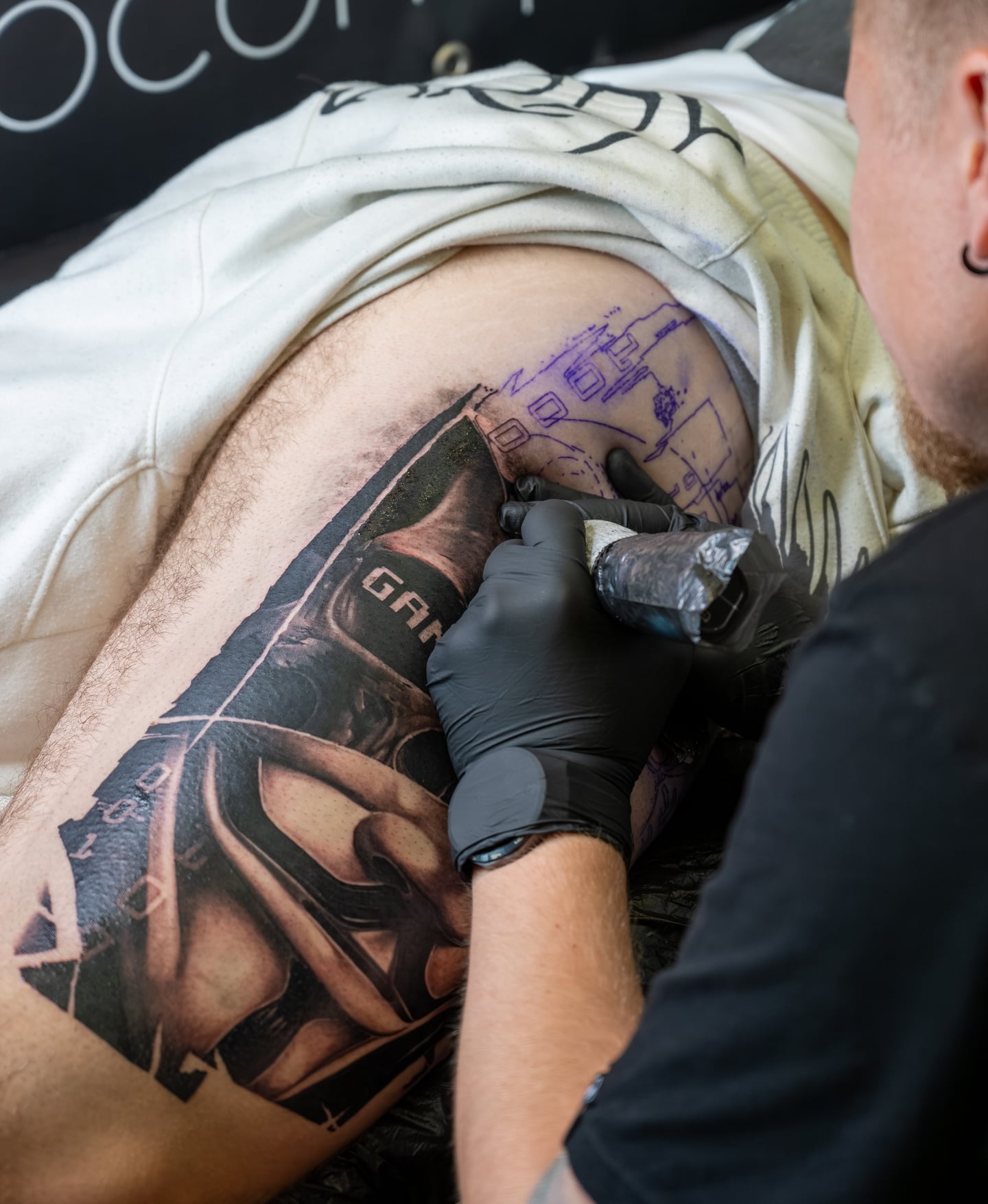 Gloved hands working on a shaded tattoo on a client's side.