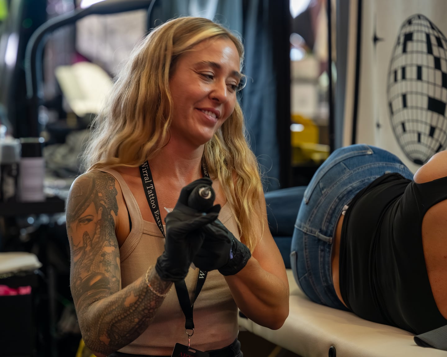 A smiling tattoo artist in black gloves holding a tattoo machine.
