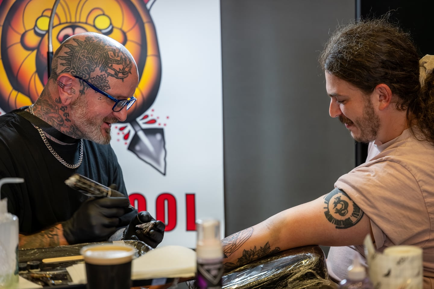 A tattoo artist working on the arm of a seated client.