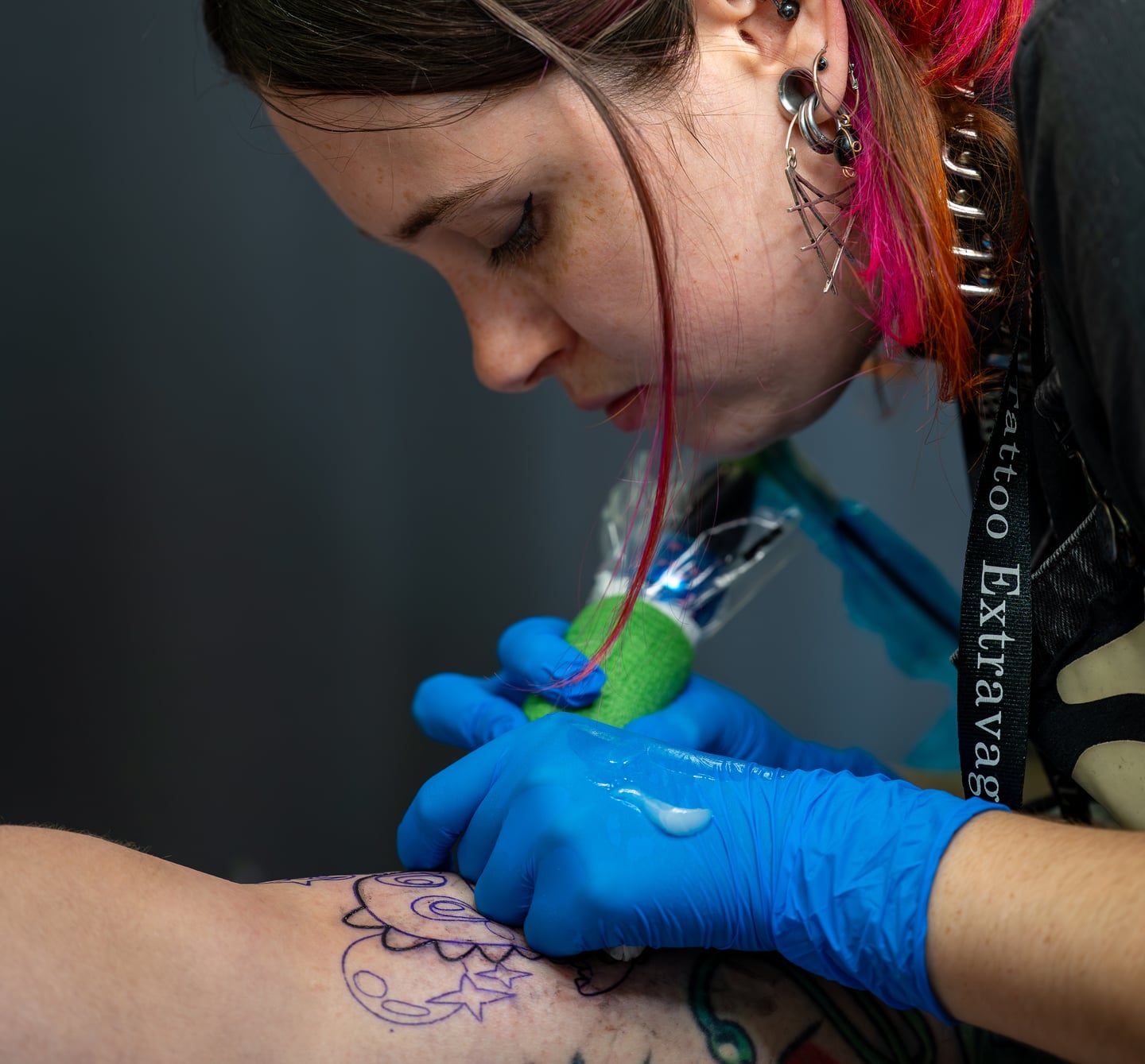 A tattoo artist in blue gloves working over a purple stencil.