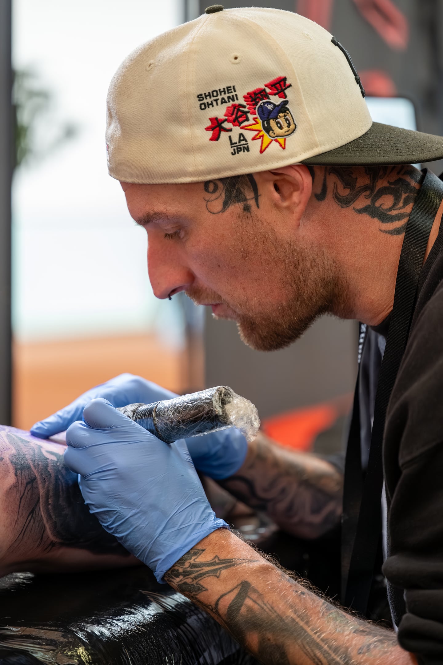 A tattoo artist wearing a white cap working with blue gloves.