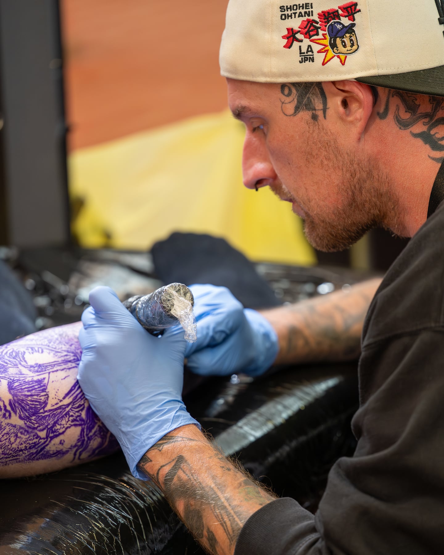 Side view of a tattoo artist in a white cap concentrating on a tattoo.