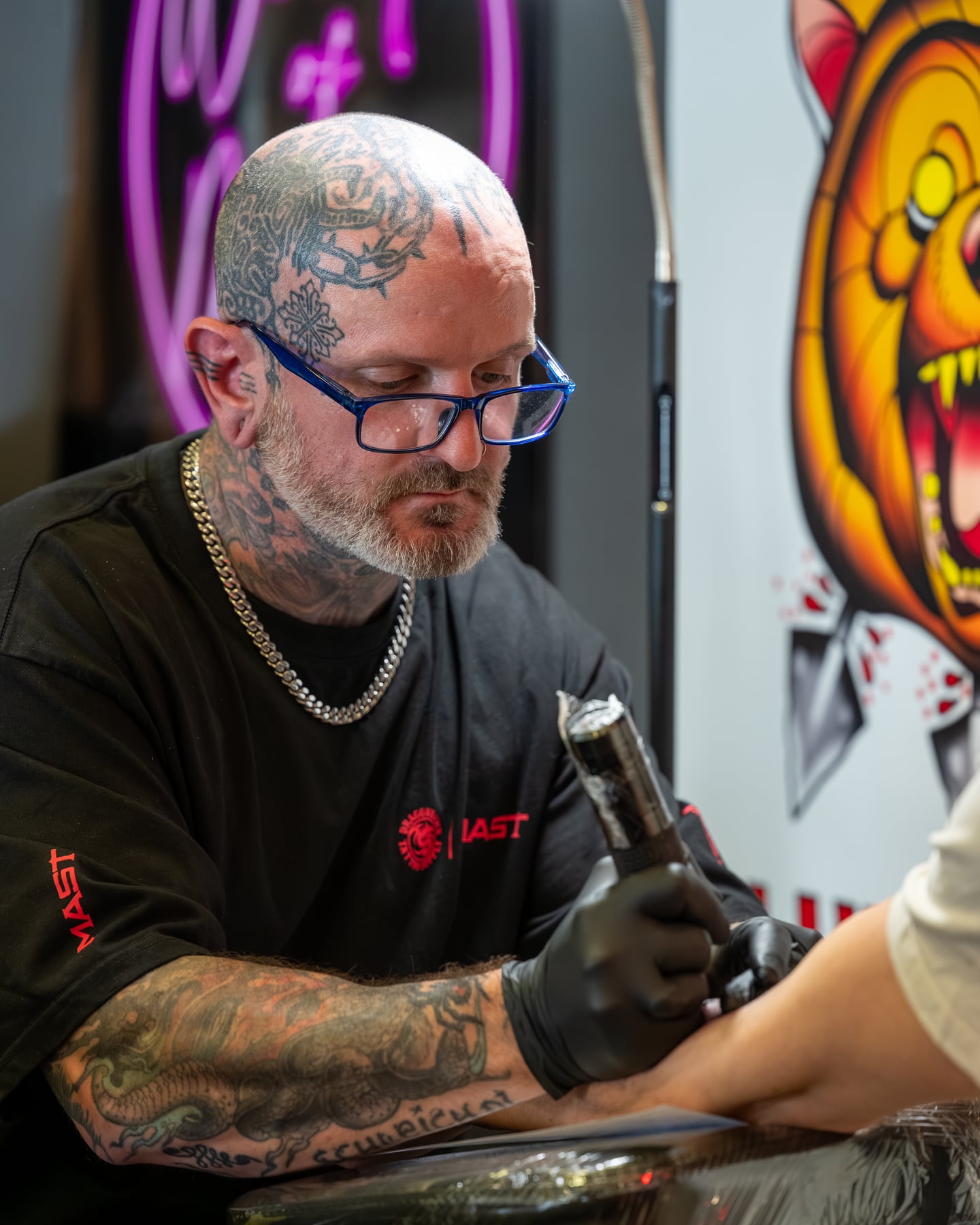 A tattoo artist with glasses working with a tattoo machine.