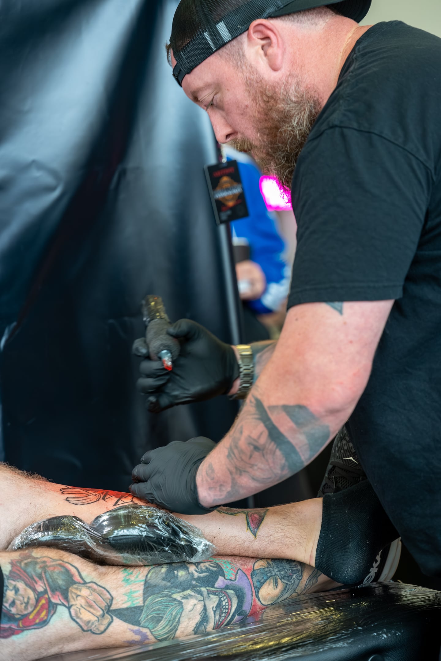 A tattoo artist leaning over a client while working on a detailed design.