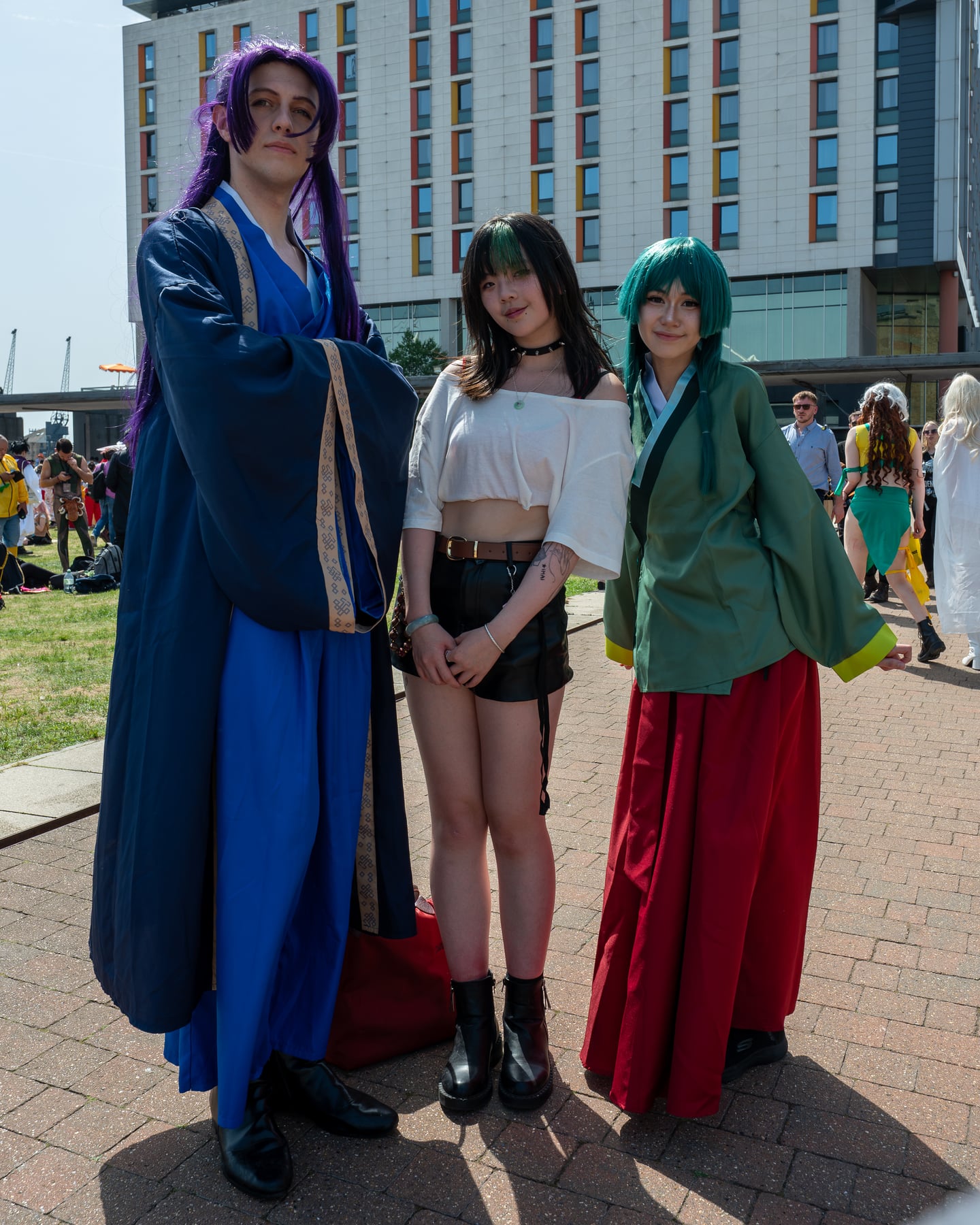 Three cosplayers posing together outside a convention venue.