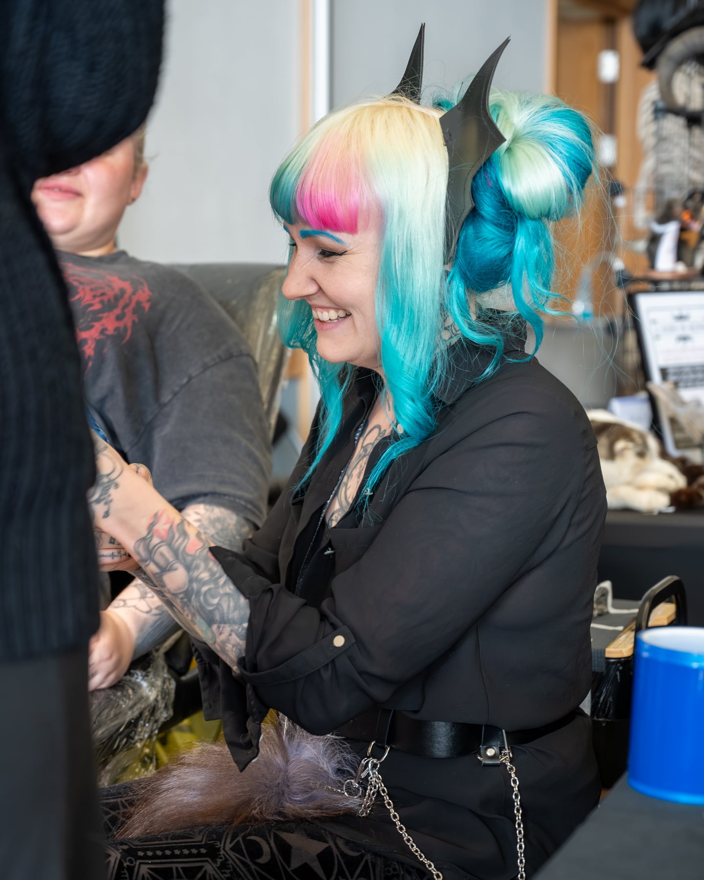 A turquoise-haired tattoo artist smiling while working at the event.