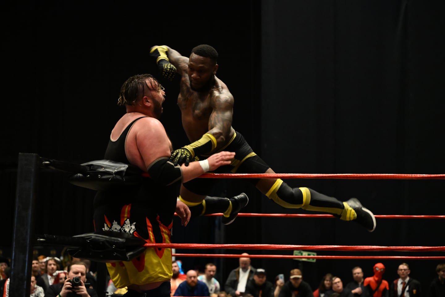 Two wrestlers in action above the ropes of a wrestling ring.