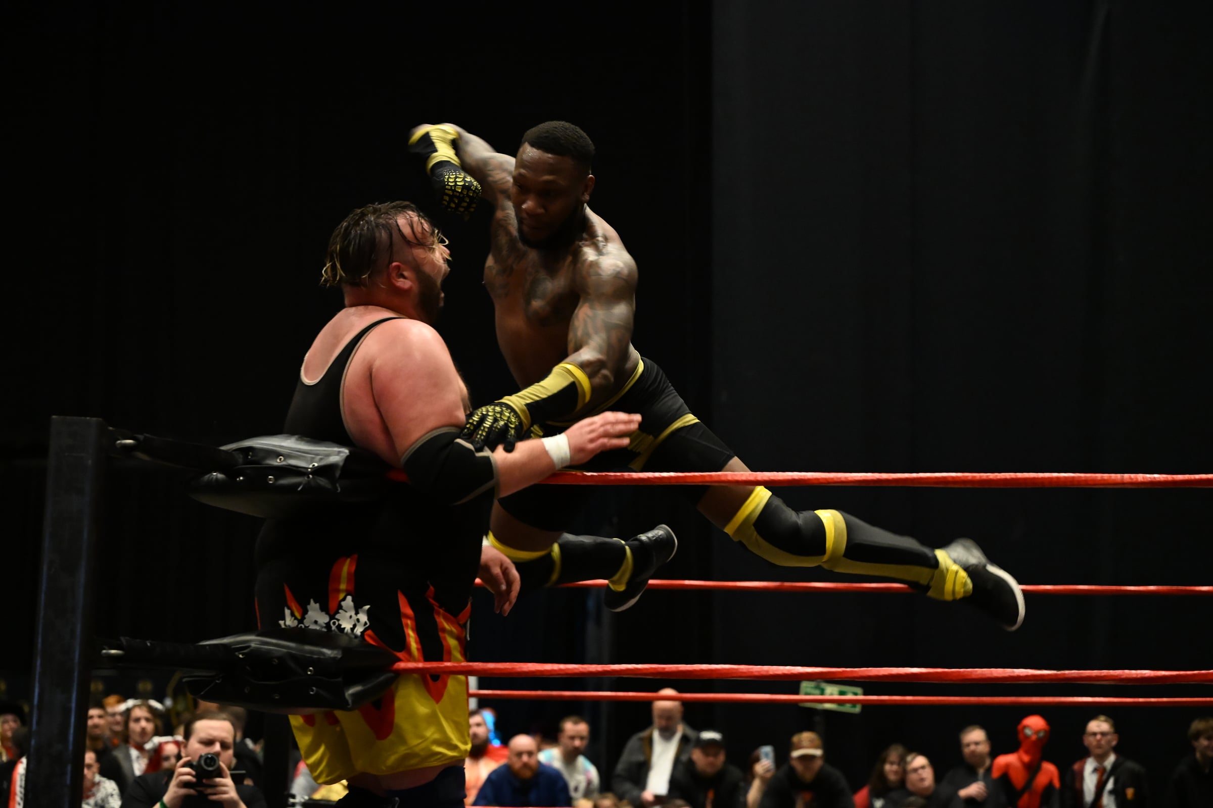 Two wrestlers in action above the ropes of a wrestling ring.
